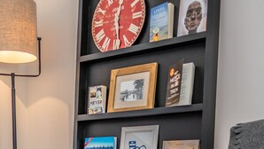 Een moderne woonkamer met een grote flatscreen-televisie, een vloerlamp en een boekenkast vol boeken en ingelijste foto's.