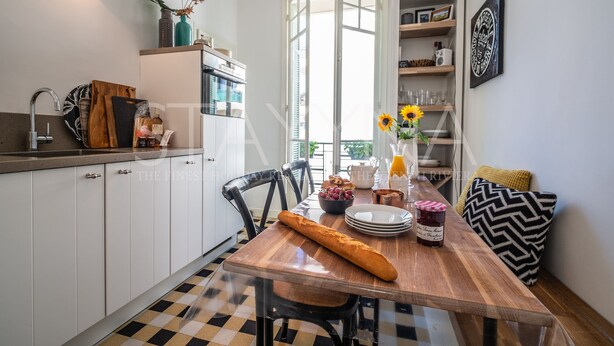 Een keuken met witte kastjes, een houten tafel en een geruit vloertje.
