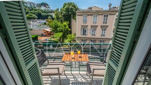 Een terras met een houten tafel en stoelen, met uitzicht op een stadsbeeld met gebouwen en bomen.