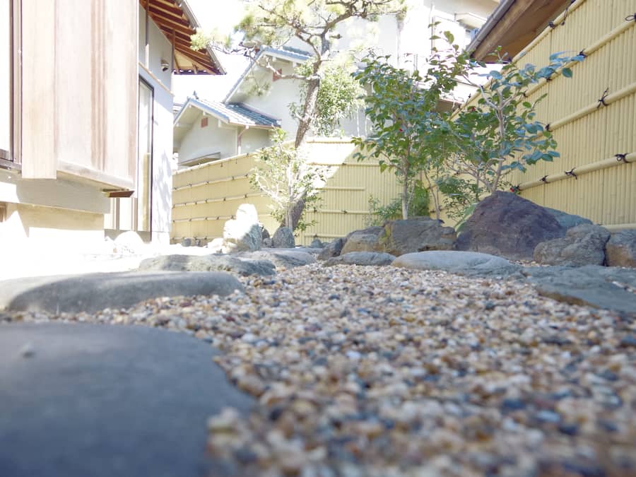 A traditional Japanese garden with a gravel path, rocks, and a small tree.