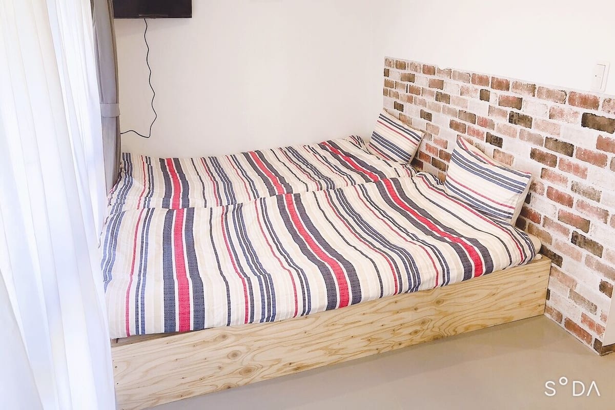 Ein Einzelbett mit einem gestreiften Bettbezug, einem hölzernen Kopfstück und einer Wand mit Backsteinoptik.