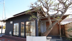 A traditional Japanese house with a tiled roof, a wooden door, and a large tree in the yard. - BOND - Hostel (Shimamoto)