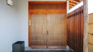 A traditional wooden door with vertical slats, a small trash bin, and a tiled floor.