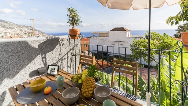 Ein Balkon mit Frühstückstisch, einem Blumentopf und Blick auf das Meer.