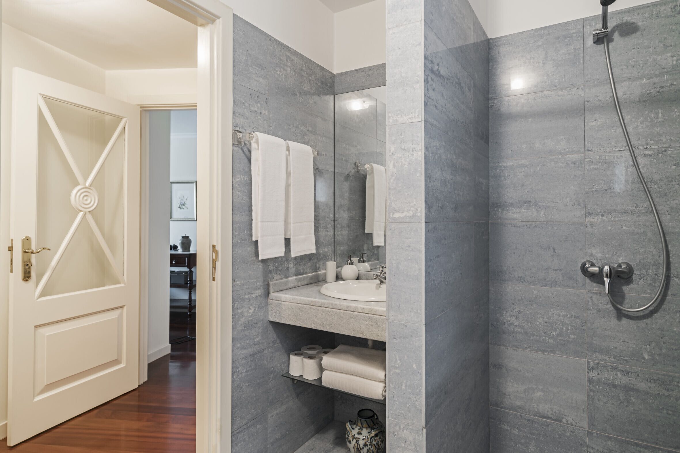 A bathroom with a sink, mirror, and shower. There are towels and toiletries on the counter.