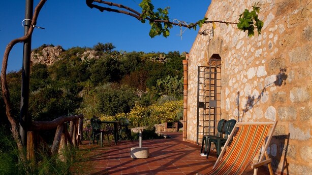 Un patio con pared de piedra, una silla de madera y una mesa.