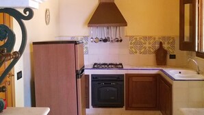 Una cocina con un arco de piedra, vigas de madera, estufa a gas, un fregadero y una estantería decorativa de metal.