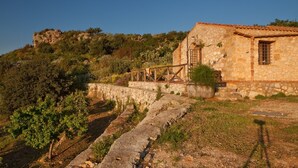 Edificio de piedra con tejado de tejas, una escalera de piedra y vistas a una colina cubierta de vegetación.