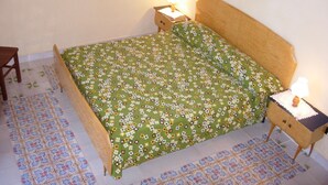 Un dormitorio con colcha verde estampada, dos lámparas de noche, una mesita de noche de madera y baldosas de suelo con diseño.
