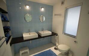 A bathroom with two sinks, a toilet, a small step stool, and a window.