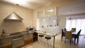 A modern kitchen with a microwave, stove, and bar stools. There is a dining area with a table and chairs. - Nightlife but quiet area, modern large home, bayview, garden, bbq, parking (St. George's Bay)