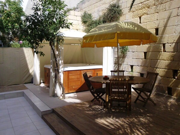 An outdoor patio with a wooden table and chairs, a yellow umbrella, and a hot tub.