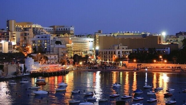 A coastal cityscape at dusk with buildings, a waterfront promenade, and boats. - Nightlife but quiet area, modern large home, bayview, garden, bbq, parking (St. George's Bay)