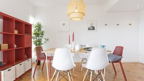 A dining area with a wooden table, white chairs, a red bookshelf, and a hanging light fixture.