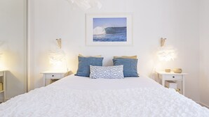 A bedroom with a large bed, white bedding, two bedside tables with lamps, and a framed picture of a wave on the wall.