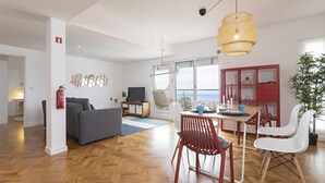 A modern living room with a sofa, dining table, and chairs, a television, and a large window with a view.