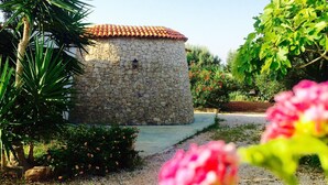A stone building with a tiled roof, surrounded by gravel, plants, and a pathway. - Trullo Sage by LoveSud (Pescoluse)