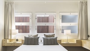 A bedroom with a large bed, two bedside tables, and three windows.