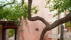 A narrow stone pathway leading to a building with a pink facade, a metal gate, and a tree with a twisted trunk. - Charming house with shared pool - Titi (Buseto Palizzolo)