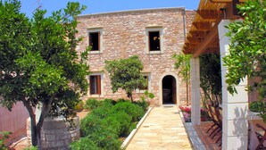 Ein Steinhaus mit einem zentralen Eingang, umgeben von Grünflächen und einem gepflasterten Weg.
