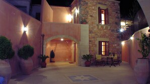 Ein zweigeschossiges Steinhaus mit einer Terrasse, die einen Tisch, Stühle, Topfpflanzen und einen Fliesenboden mit Sternenmuster zeigt.