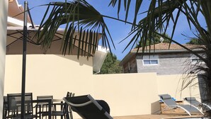 Una terraza de madera con sillones y una mesa, rodeada de palmeras y un cielo despejado.