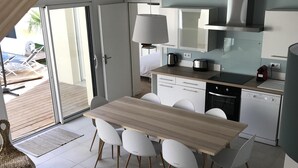 Una cocina moderna con una mesa de madera y sillas blancas, horno empotrado y un amplio ventanal con vistas a una piscina.