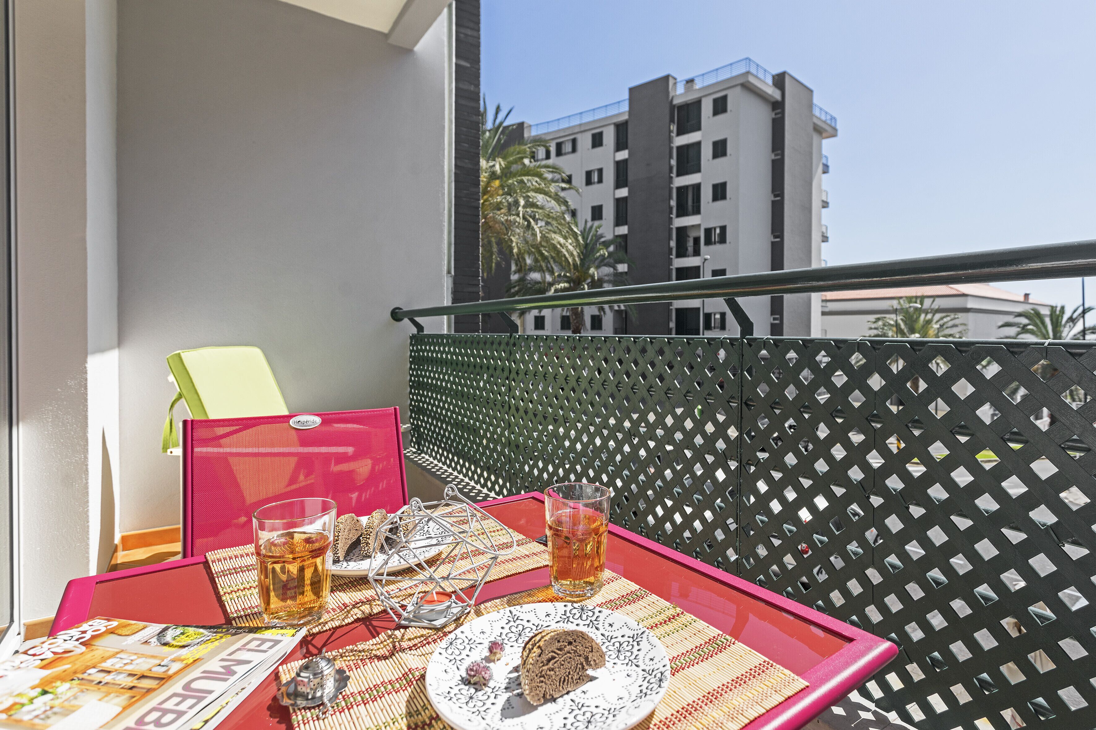 A balcony with a table set for two, featuring a tray with a glass of beverage, a plate with cookies, and a magazine.