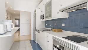 Une cuisine moderne avec des meubles blancs, un four à micro-ondes encastré, un réfrigérateur en acier inoxydable et une plaque de cuisson à induction noire.