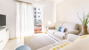 Un salon moderne avec un canapé, un téléviseur et un balcon agrémenté d’une chaise rouge.