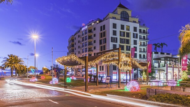 Un hôtel à plusieurs étages, doté d’une entrée imposante, d’un espace extérieur aménagé pour s’asseoir et de décorations festives.
