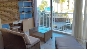 Une chambre avec un balcon, des meubles en osier, un petit bureau et des étagères.