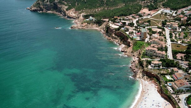 Une ville côtière avec une plage, des maisons et une chaîne de montagnes en arrière-plan.