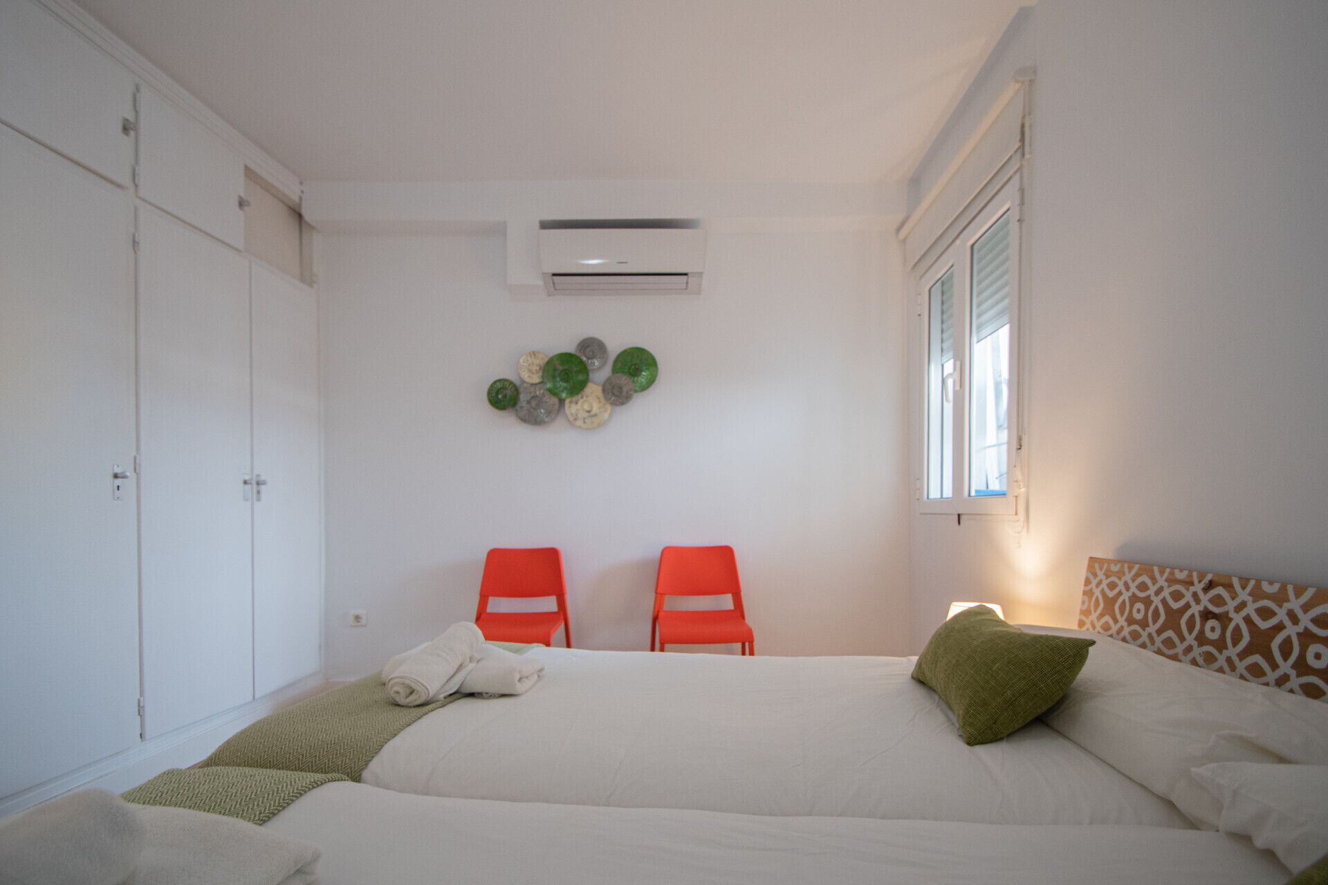 Une chambre à coucher comprenant un lit, deux chaises, un climatiseur fixé au mur et une fenêtre avec des stores.