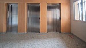 Tres puertas de ascensor en una habitación con suelo de granito y una ventana a la derecha.
