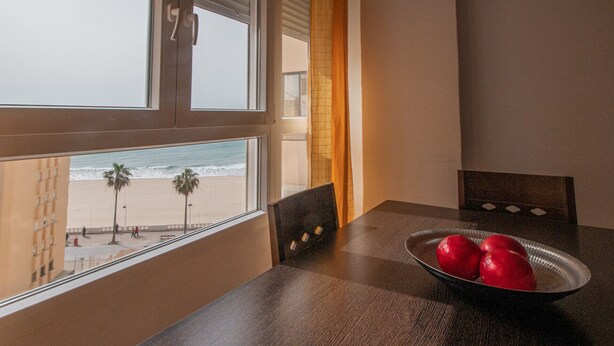 Una habitación con una mesa de madera, un cuenco de manzanas rojas y vista al mar a través de una ventana.