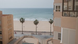 Vista a la playa desde un balcón con palmeras y cielo despejado.