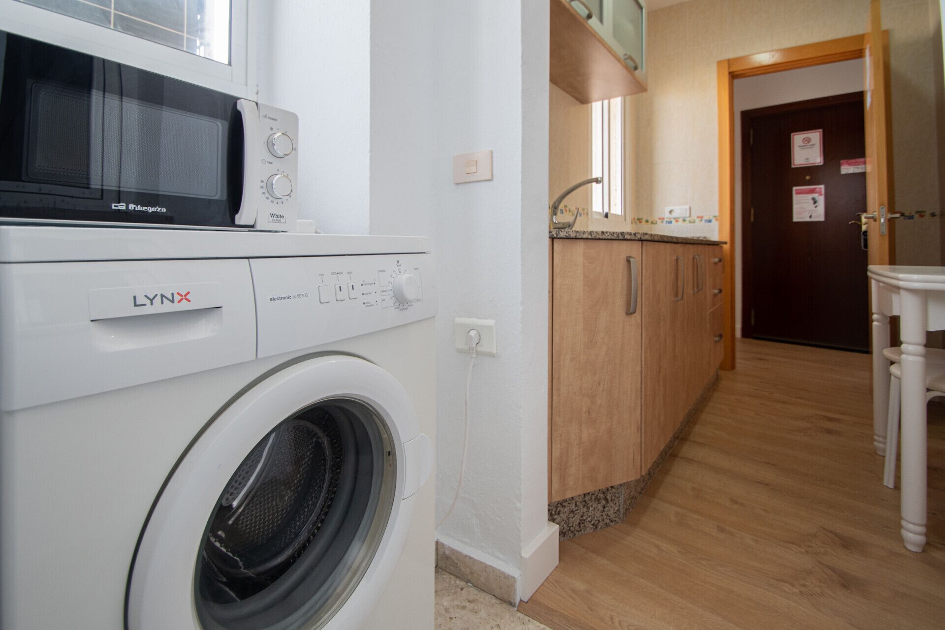 Un espace buanderie comprenant un lave-linge LYNX blanc, un four à micro-ondes et des armoires en bois.