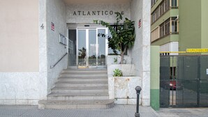 Entrada de un edificio con fachada de mármol, una escalera que lleva a una puerta de cristal y un letrero que dice "ATLANTICO 6".