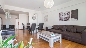 A modern living room with a brown leather sofa, a white coffee table, and a dining area with a white table and chairs. - Rodamar I, the promenade, the beach and a sea view (Funchal)