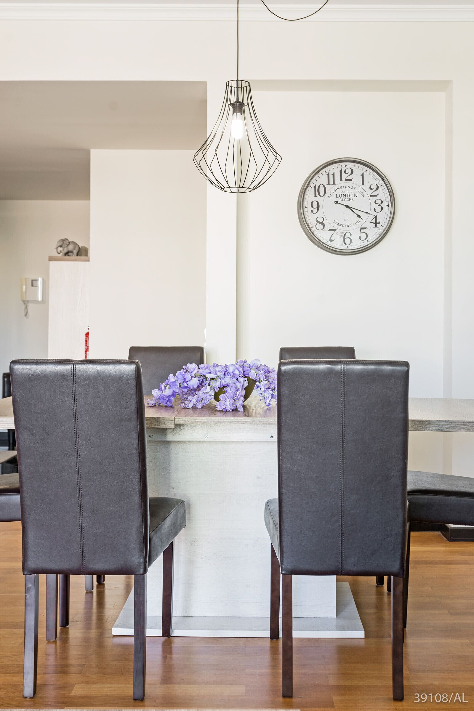 A dining area with a table, chairs, a clock, and a pendant light.