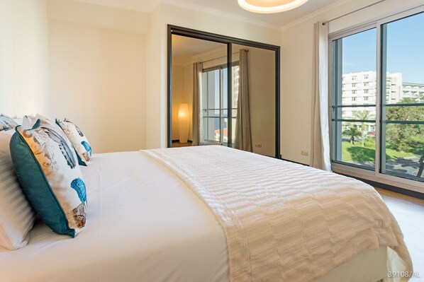 A hotel room with a large bed, a wardrobe, and a window with a view of buildings and greenery.