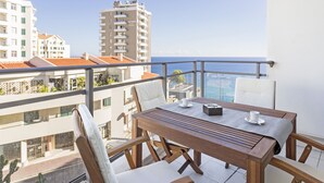 A balcony with a wooden table and chairs, overlooking a cityscape and the sea. - Rodamar I, the promenade, the beach and a sea view (Funchal)