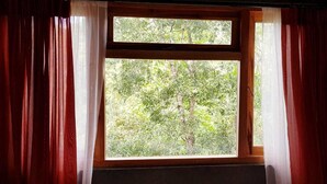 A window with a view of trees outside, framed by red curtains. - Tea Leaf Retreat Peradeniya (Doluwa)