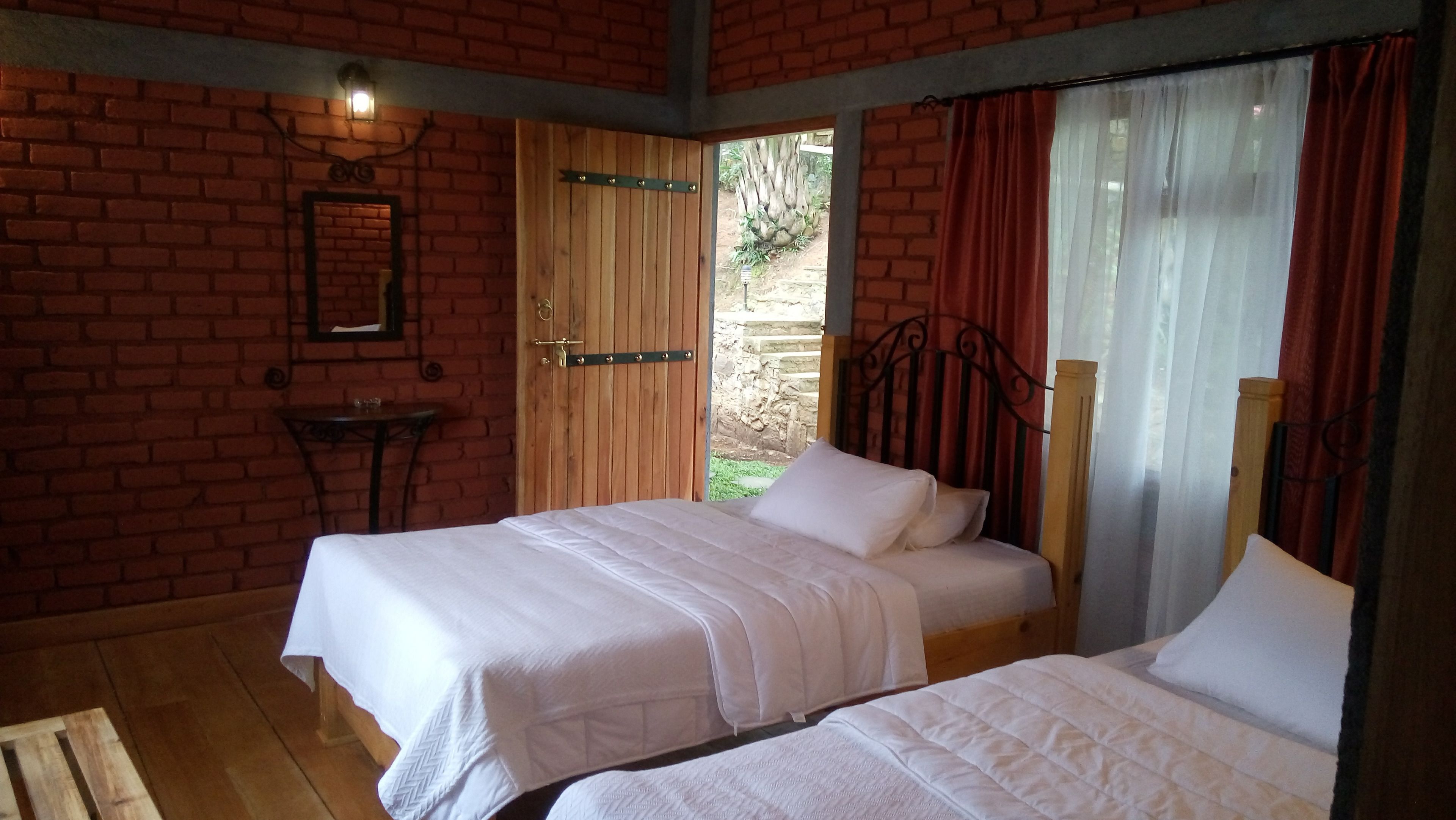 A room with two beds, a wooden door, a small table, and a brick wall.