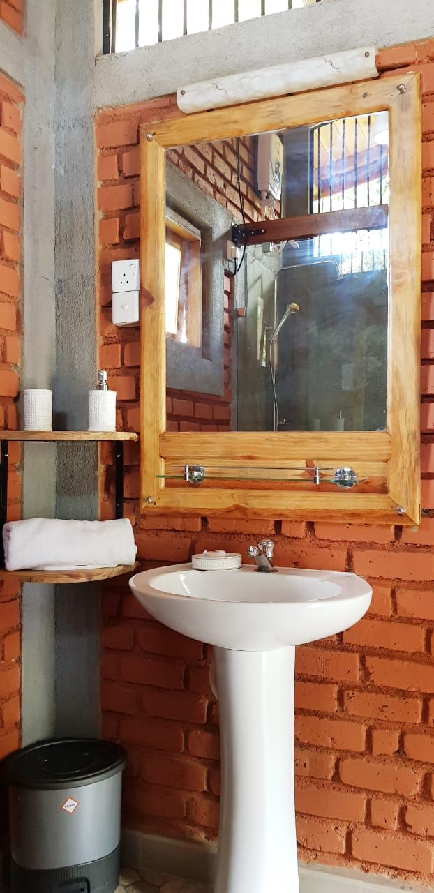 A bathroom with a white sink, a wooden-framed mirror, and a brick wall.