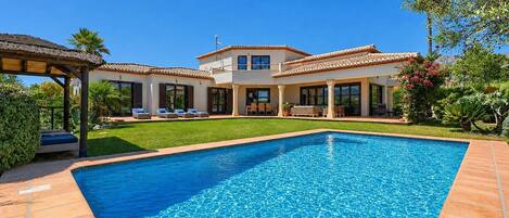 Una casa de dos pisos con piscina, un patio con mobiliario exterior y un jardín bien cuidado.