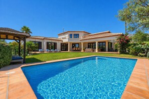 Une maison à deux étages avec une piscine, un patio doté de mobilier d’extérieur et un jardin bien entretenu.