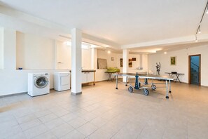 A spacious living area with a ping pong table, washing machines, and a dining table.