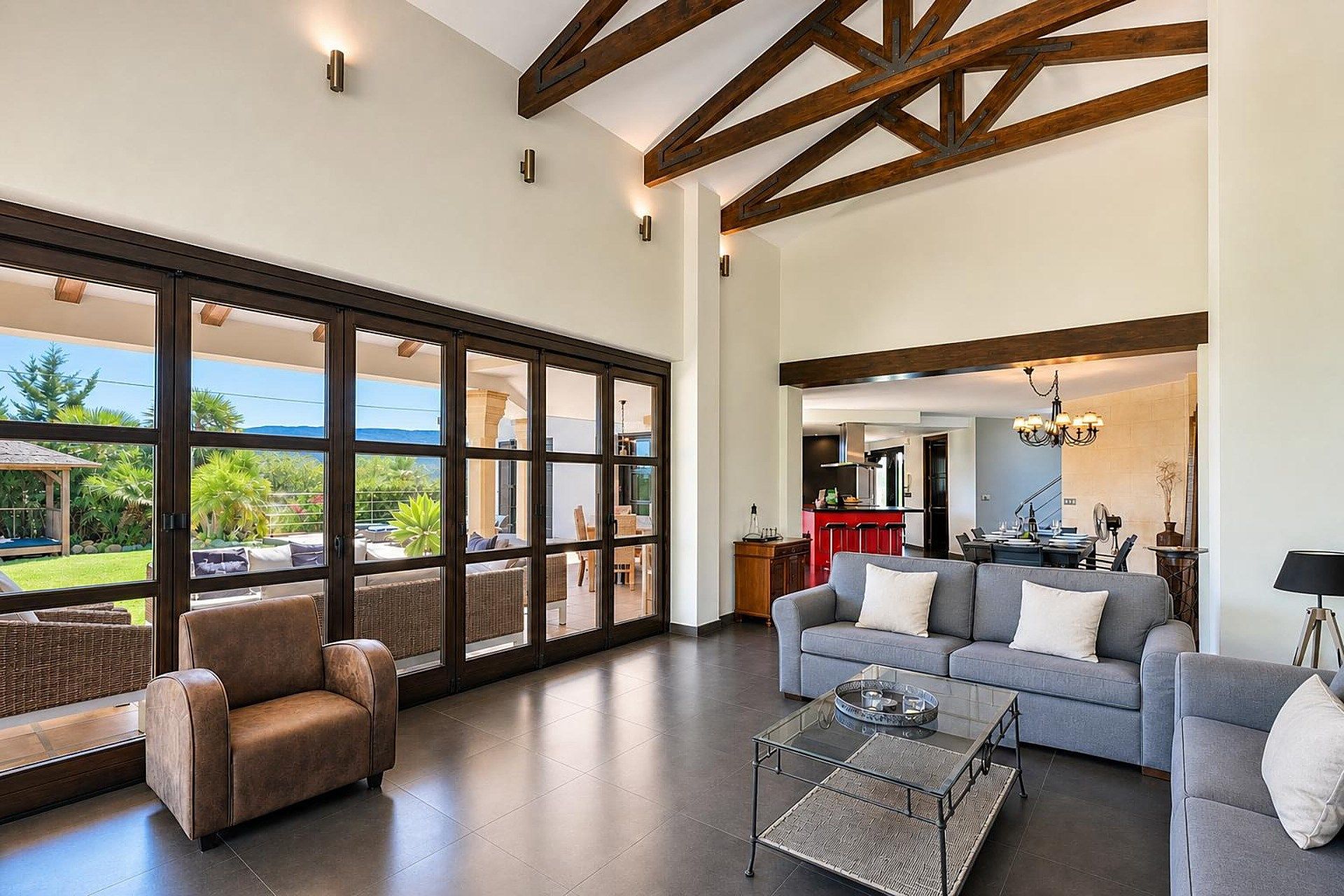 A spacious living area with a large glass door leading to an outdoor patio, a grey sofa, a brown leather armchair, and a glass coffee table.